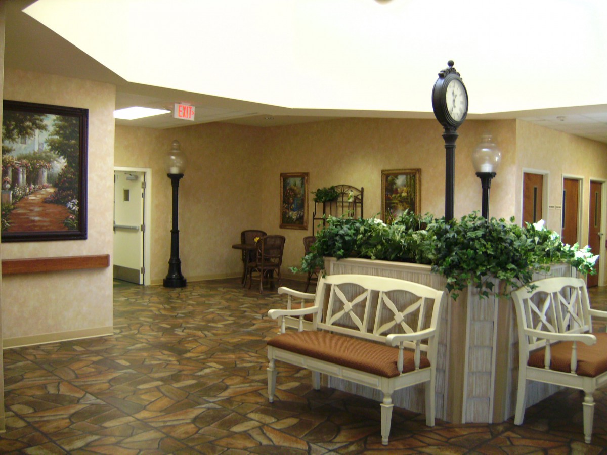 A warmly lit hallway with benches, decorative plants, and a clock.