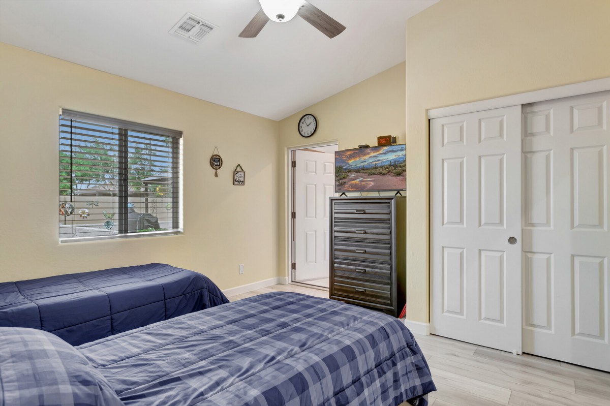 A tidy bedroom with twin beds covered in blue plaid bedspreads, a wooden dresser, and a closet with double doors.