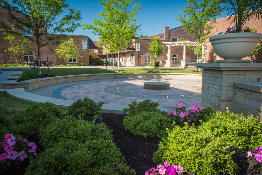 A serene university campus courtyard with manicured gardens and traditional architecture under a clear blue sky.