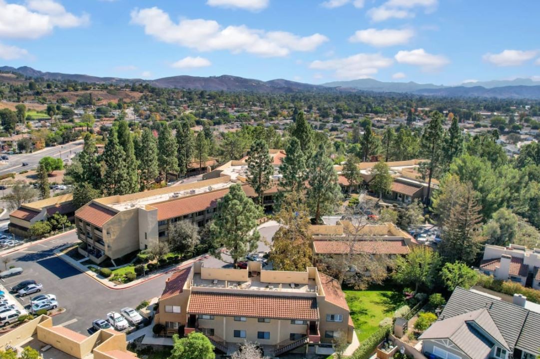 Aerial view of a suburban area with buildings surrounded by trees under a partly cloudy sky.