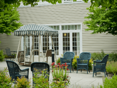 A cozy outdoor patio area featuring a swing, multiple chairs, and lush greenery.