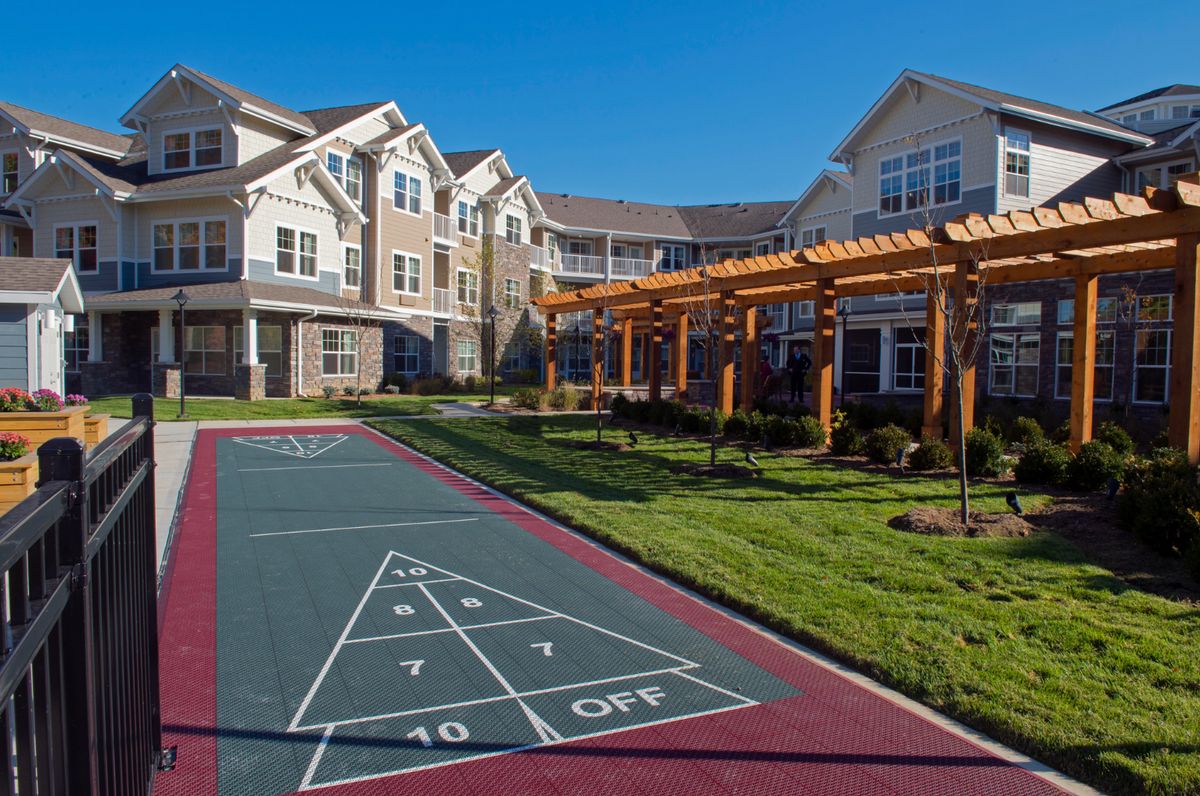 A sunny day view of a residential building with an outdoor shuffleboard court and a pergola.