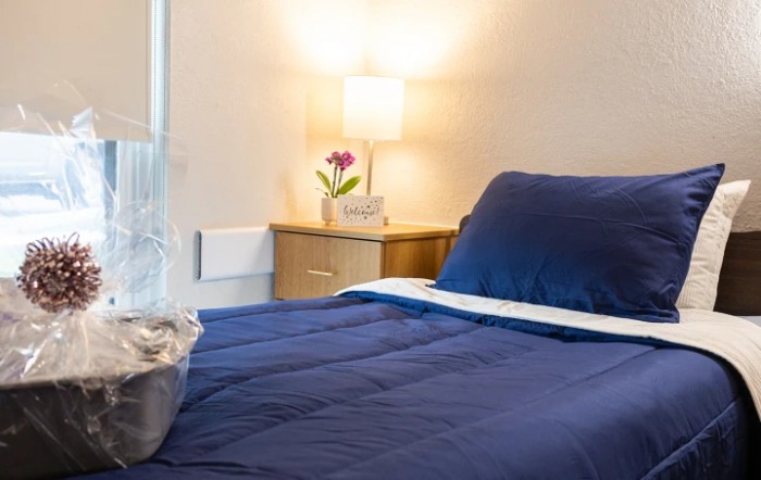 A cozy bedroom with a neatly made bed, a nightstand, and a lit lamp.