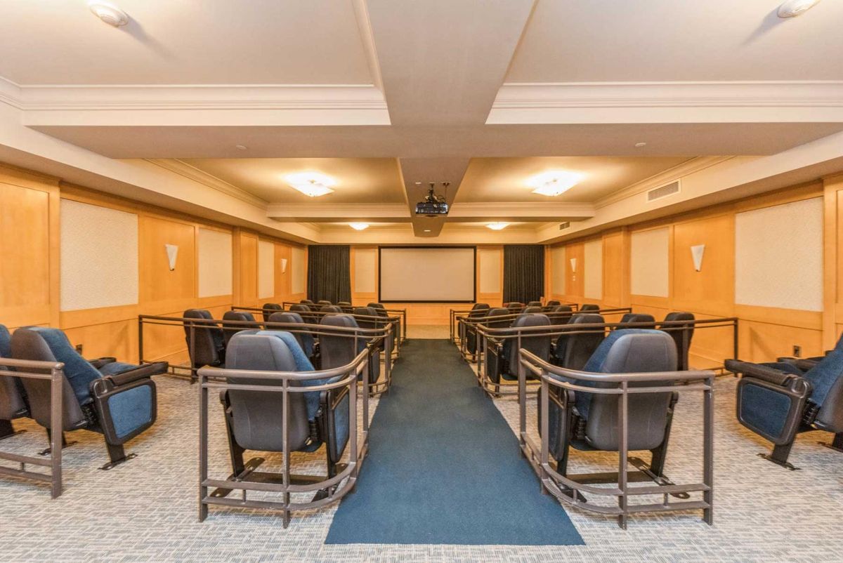 An empty theater room with rows of seats facing a projection screen.
