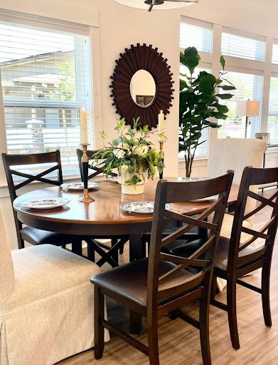 A stylish dining area featuring a round wooden table, elegant chairs, a decorative mirror, and greenery.