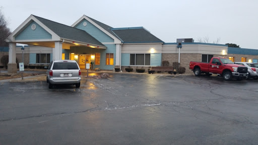 A view of a hotel entrance in the evening, featuring parked cars and a cloudy sky.