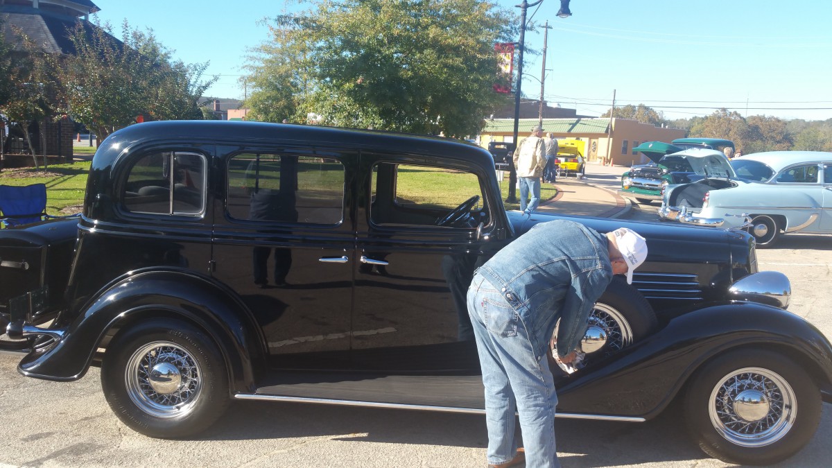 A man tends to a vintage car parked outdoors.