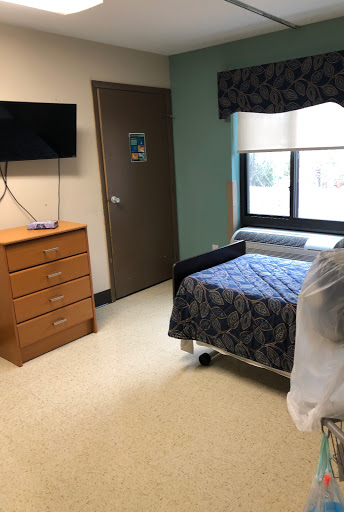 A hospital room featuring a patient bed, dresser, and television, with natural light coming through the window.