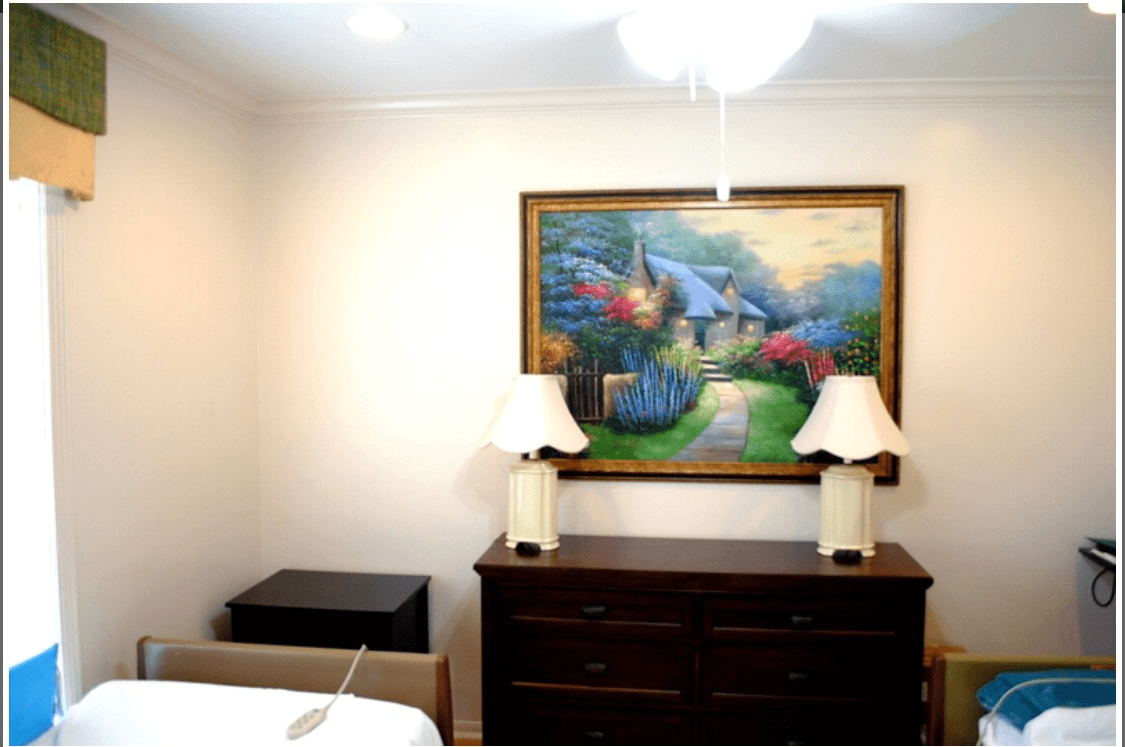 A bedroom with a dresser, two lamps, and a colorful landscape painting on the wall.