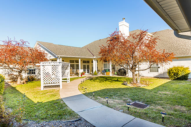 A charming house with a landscaped backyard featuring autumn-colored trees and a patio.