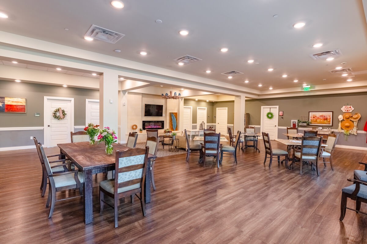 A modern dining area with wood flooring and ample seating, featuring warm indoor lighting.