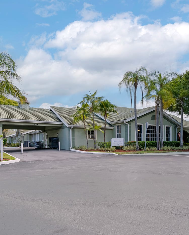 A suburban residential building with palm trees and a driveway under a cloudy sky.
