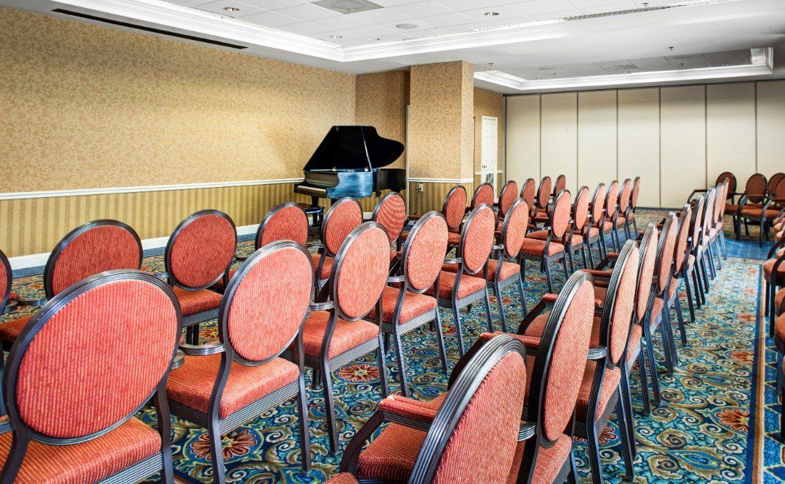 An empty conference room with rows of chairs and a piano in the corner.