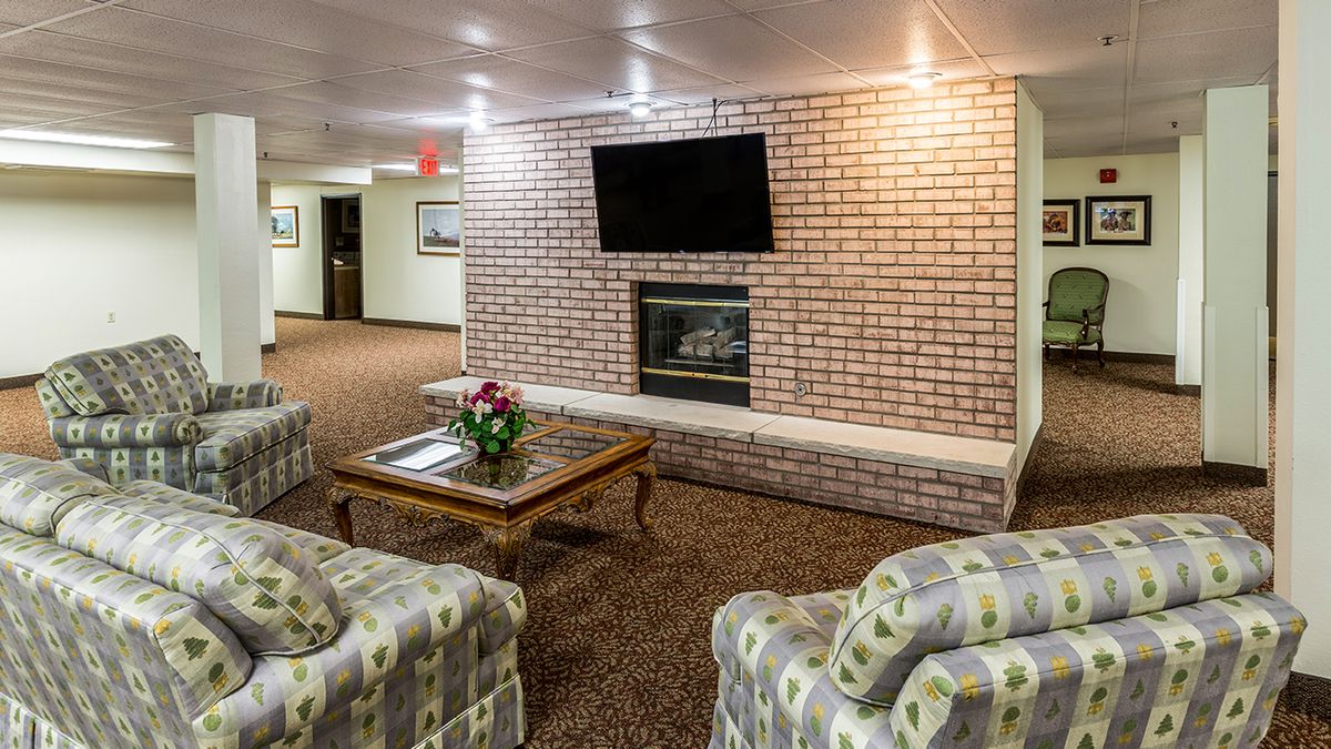 A cozy seating area with a brick wall featuring a fireplace and a mounted television, surrounded by comfortable chairs and a coffee table with flowers.