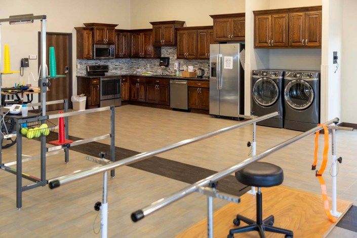 A modern kitchen combined with a rehabilitation therapy area, featuring parallel bars and appliances.