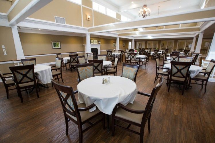 A spacious dining hall with elegantly set tables covered in white tablecloths, surrounded by wooden chairs on a polished wooden floor.