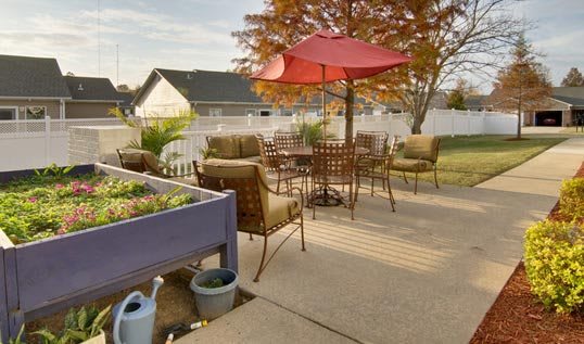 A cozy backyard patio with furniture and a red umbrella, set against an autumn backdrop.