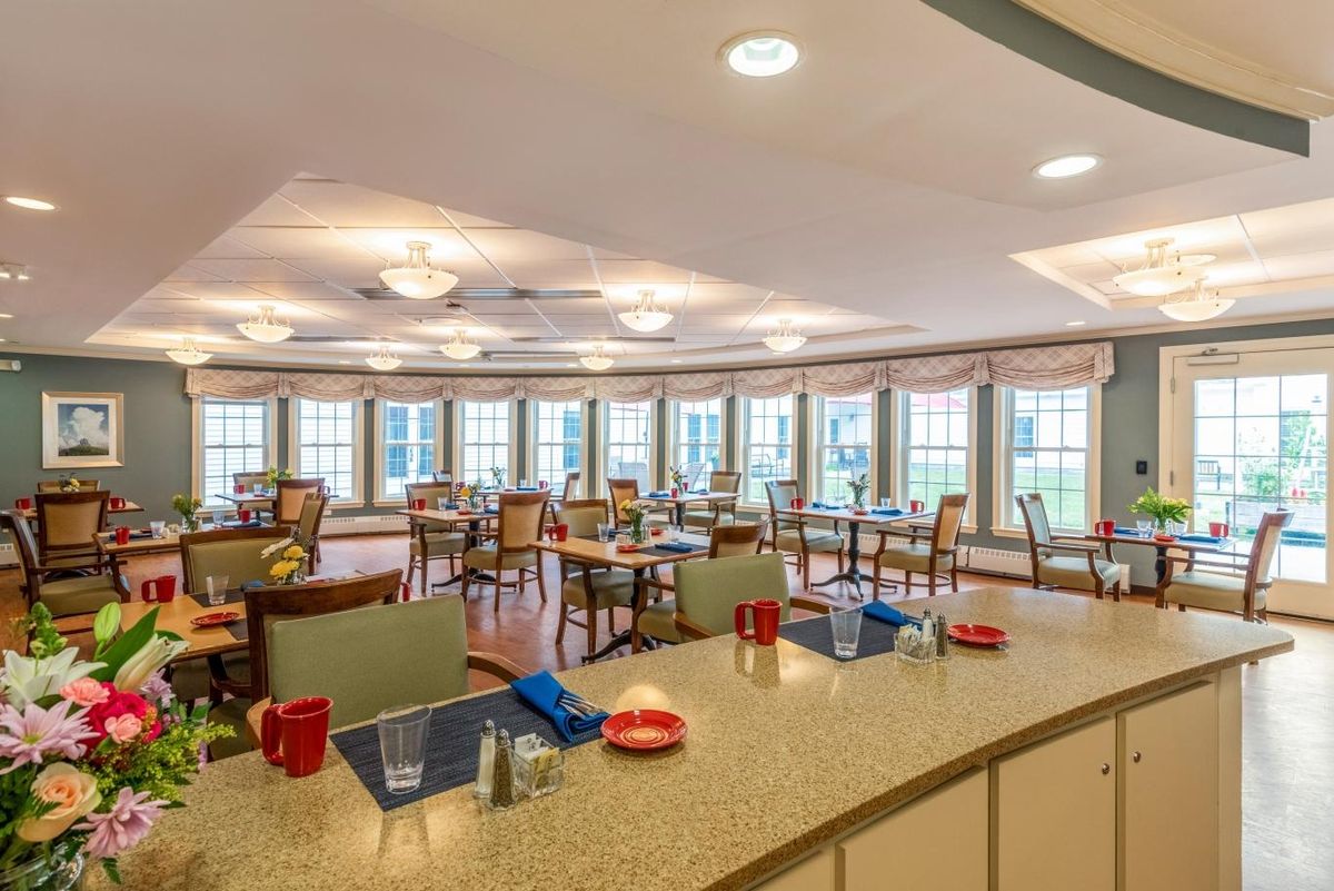 A cozy dining room with multiple tables and large windows letting in natural light.
