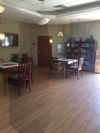 A cozy dining area featuring wooden tables and chairs, complemented by a bookshelf and warm lighting.