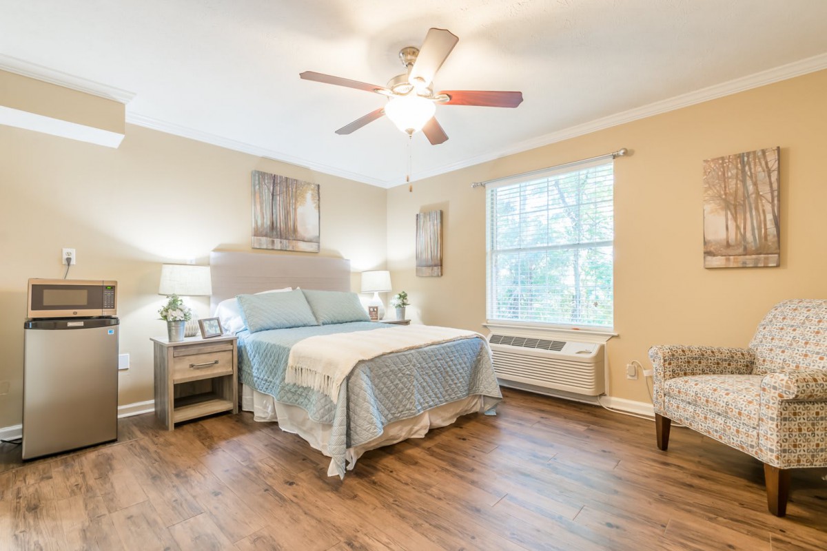 A cozy bedroom with hardwood flooring, featuring a bed with light blue bedding, two bedside tables with lamps, and a ceiling fan.