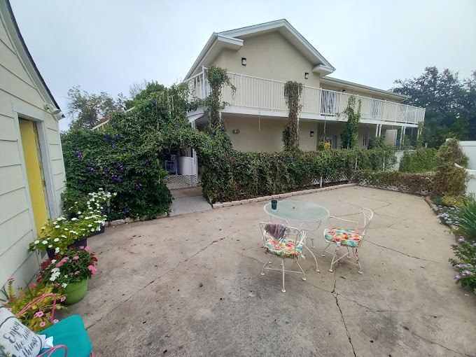 A spacious patio with outdoor furniture in front of a two-story house surrounded by lush greenery.