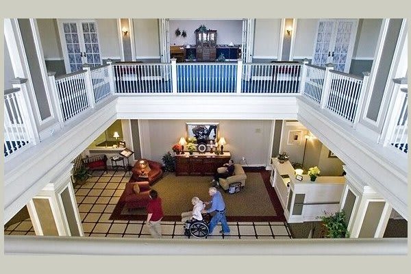 A spacious lobby in a nursing home with people, including one in a wheelchair, moving through the area.