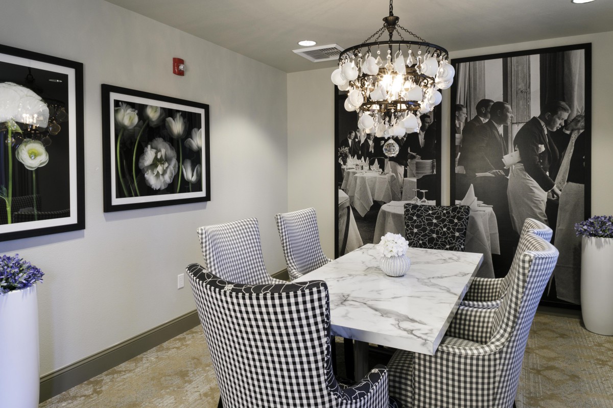 A modern dining room with a marble table, checkered chairs, and black and white artwork on the walls.