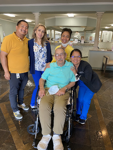 A cheerful group of caregivers posing with an elderly man in a wheelchair at a healthcare facility.