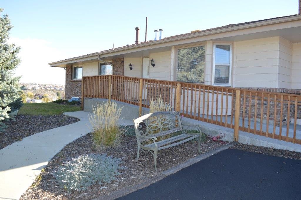 A house with a wooden ramp and metal bench surrounded by landscaped gardens.