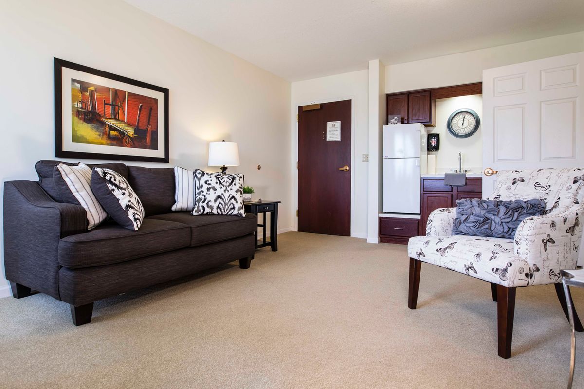 A cozy living room with a sofa, armchair, and a small kitchen area in the background.