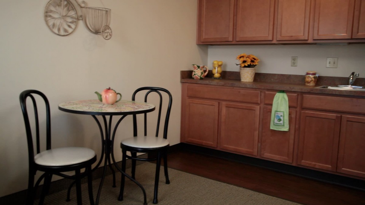 A cozy kitchen corner with a small table and chairs, adorned with a teapot and floral decorations.