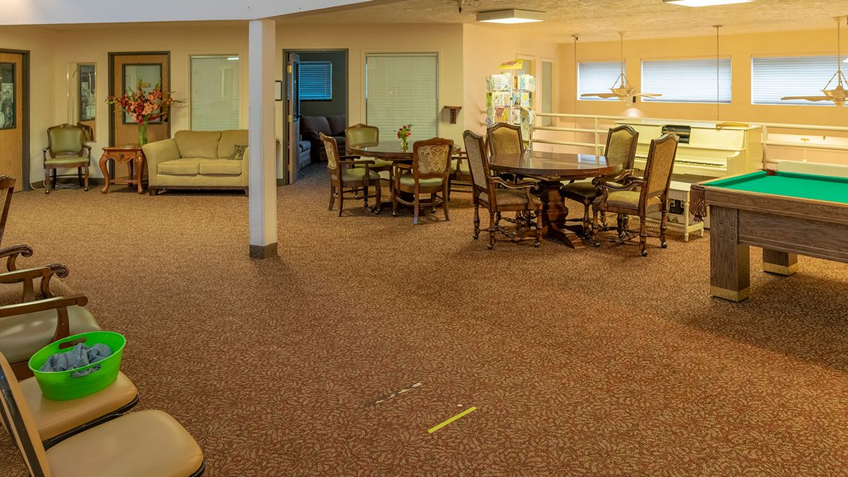 A cozy interior space featuring a seating area with wooden dining tables and chairs on a carpeted floor.