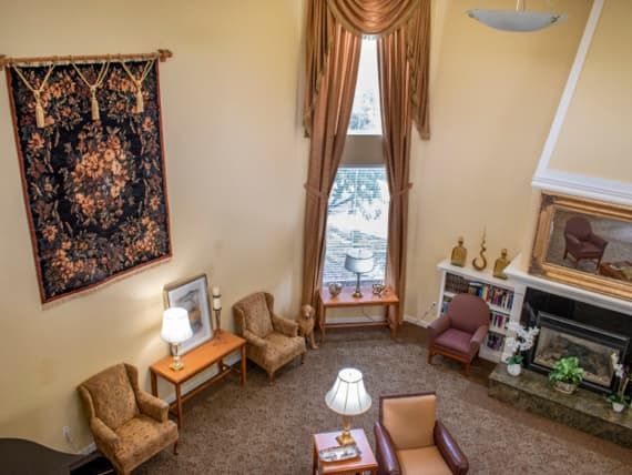 A cozy living room with elegant decor, featuring plush armchairs, a patterned carpet, and a large window with drapes.