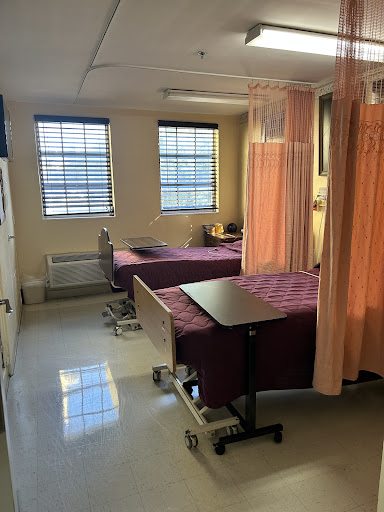 A view of a hospital patient room featuring two beds separated by curtains, with natural light coming through the windows.