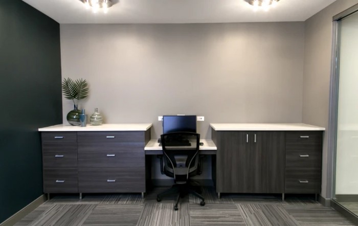 A minimalist office setup with a desk, chair, and computer between two cabinets.