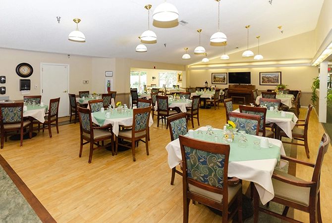 A well-lit dining room with multiple set tables and chairs on a wooden floor.