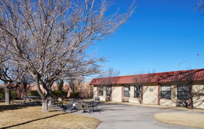 A park area featuring a building with a red roof, benches, and leafless trees under a clear blue sky.