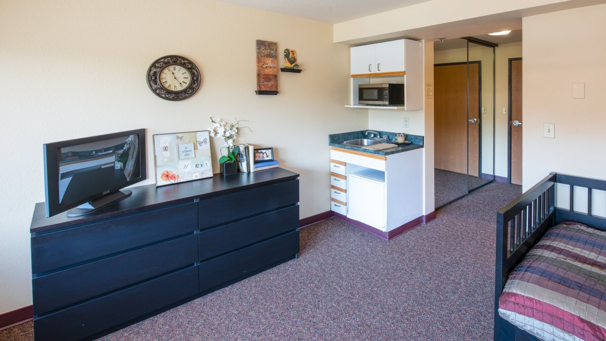 A compact studio apartment with a small kitchenette and a dresser, featuring minimalist decor.
