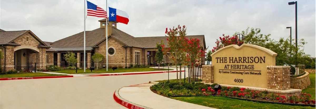 A building with a Texas flag in front, surrounded by landscaping and a cloudy sky.