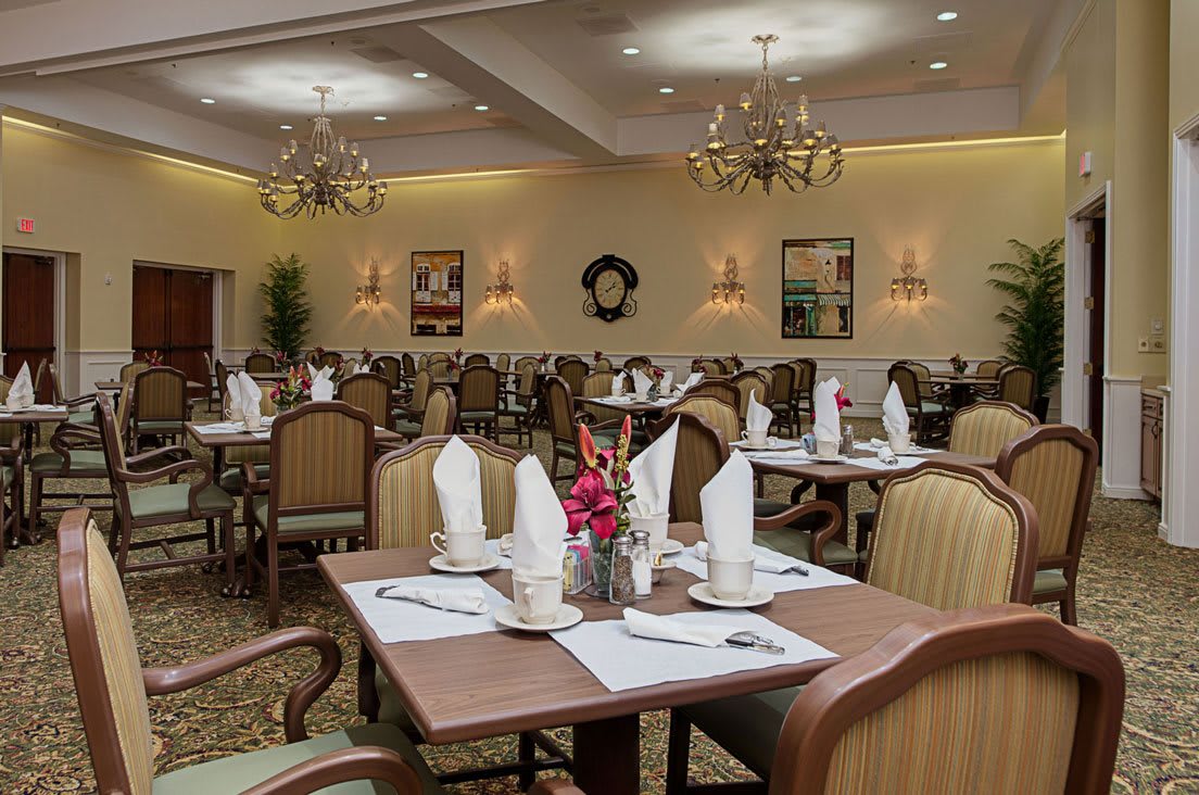 An elegantly arranged dining room with neatly set tables and chandeliers.