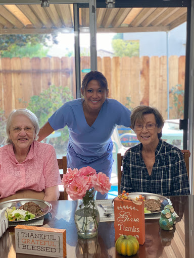 A warm gathering over lunch with seniors and their caregiver, enjoying meals and flowers.