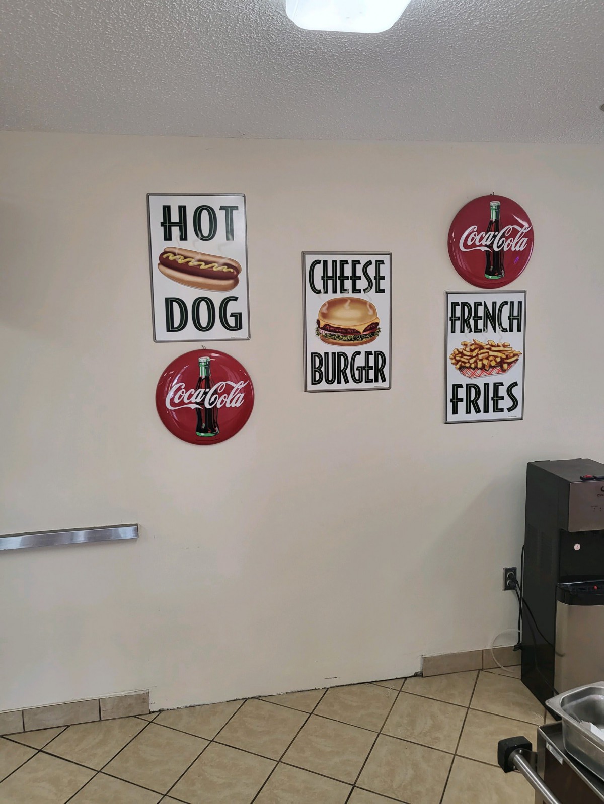 Wall decor featuring signs for hot dogs, cheeseburgers, french fries, and Coca-Cola in a restaurant.