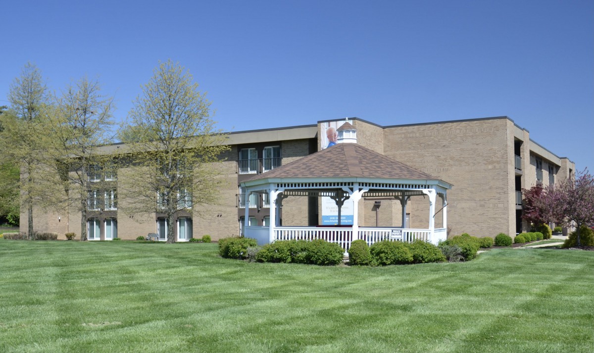 A white gazebo on a well-maintained lawn in front of a brick building under a clear blue sky.