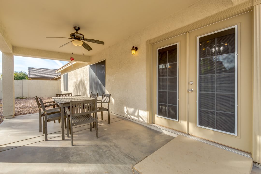 A cozy patio area featuring a dining set under a ceiling fan, with sunlight streaming through the glass doors.