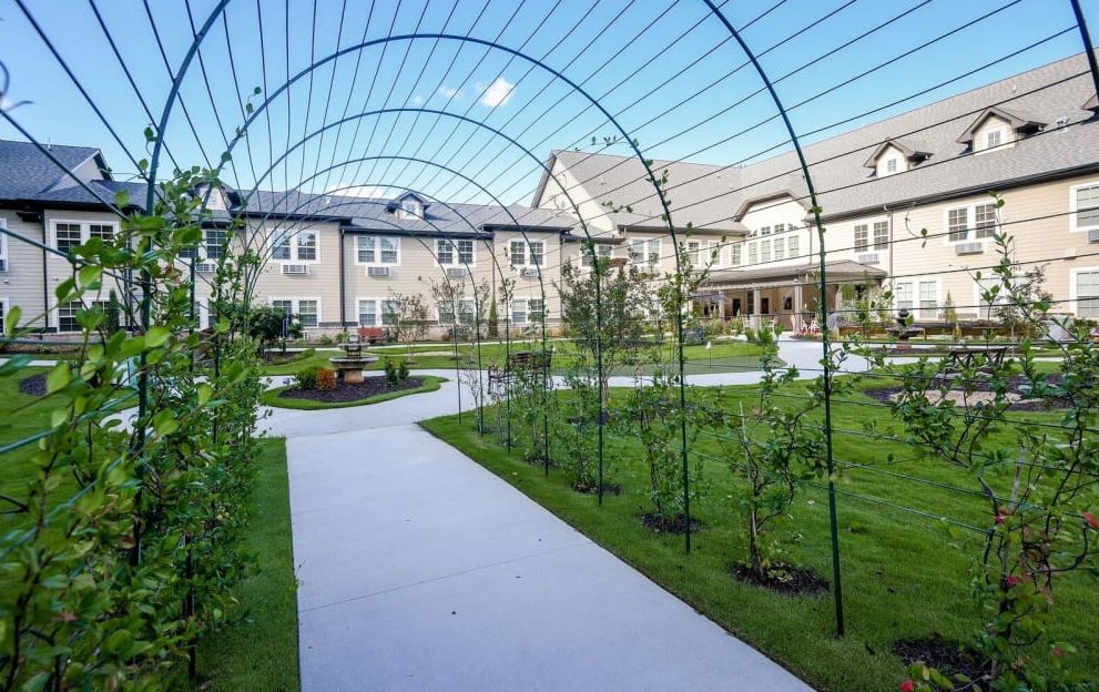 A scenic garden pathway with archways leading to a residential building.