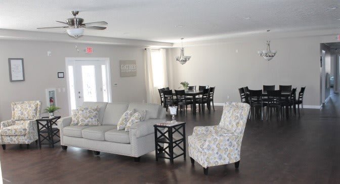 A modern living room with a comfortable sofa and chairs, a dining area in the background.