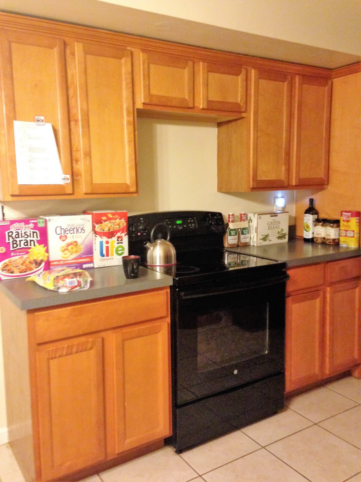 A kitchen with wooden cabinets, a black stove, and various cereal boxes on the countertop.