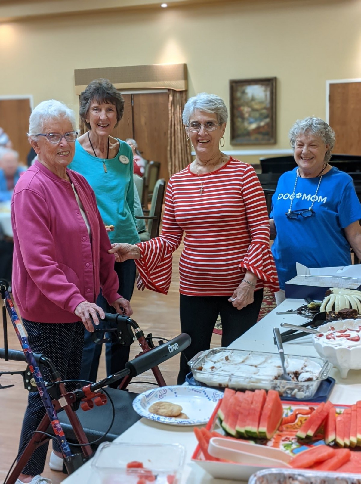 A group of elderly women enjoying a social gathering indoors, with a table in front of them.
