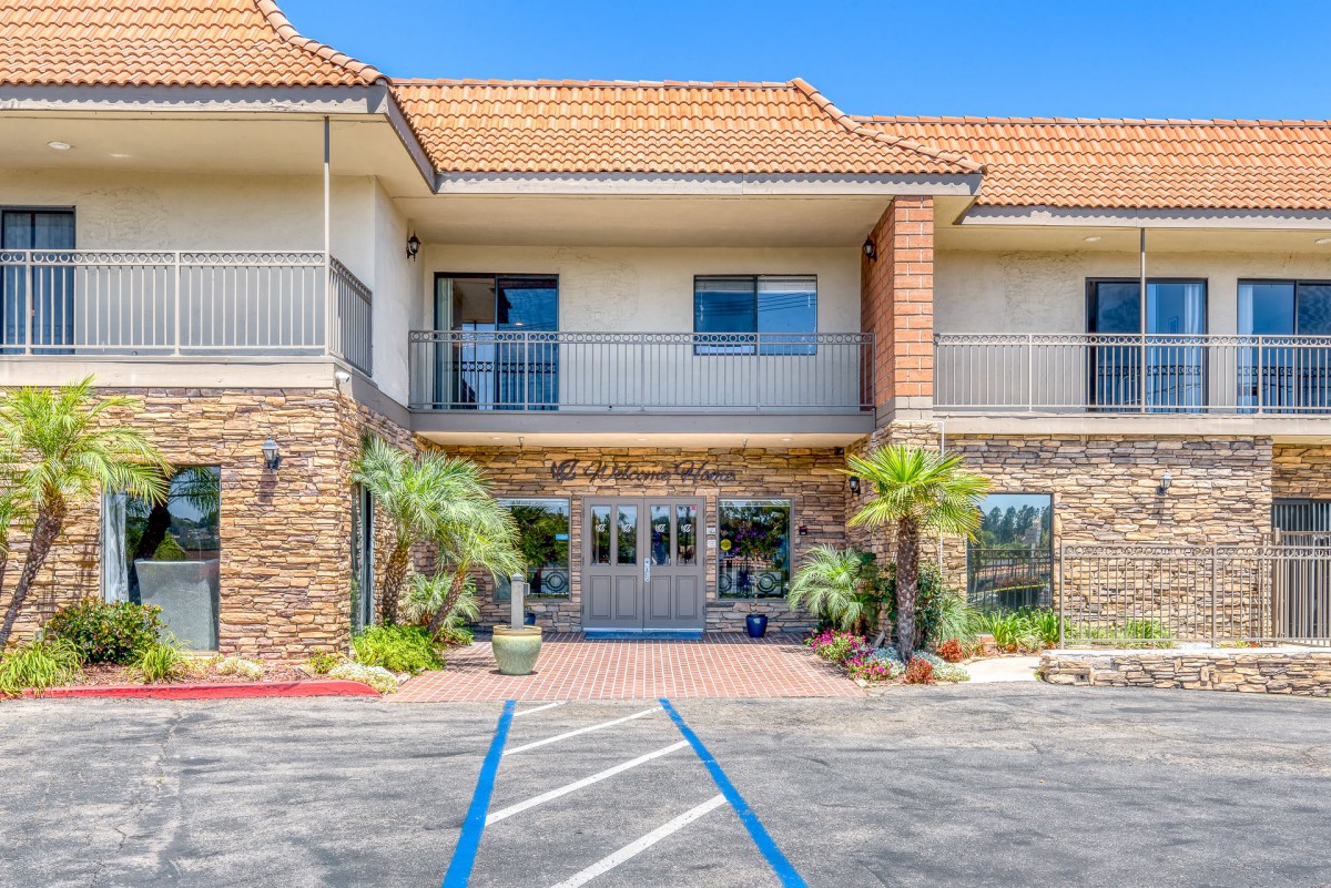 A hotel entrance with palm trees and a parking lot.