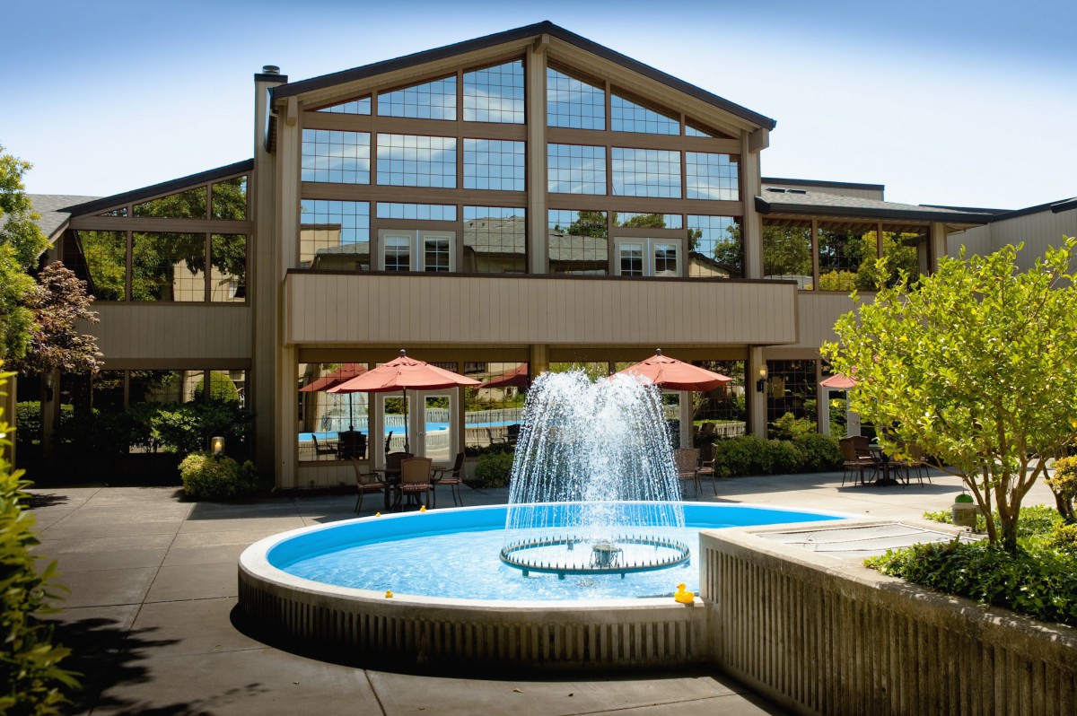 A modern building with large glass windows and an outdoor patio featuring a circular fountain.